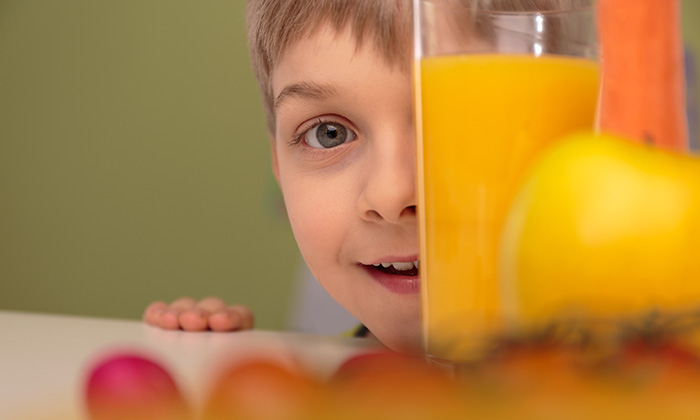 boy with face behind glass of orange juice