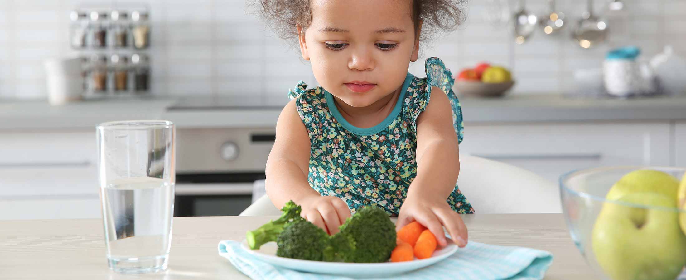 little girl sitting with water glass and veggies