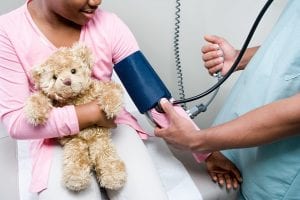 Child holding teddy bear getting their blood pressure read by a doctor