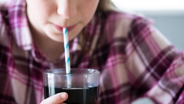 Girl drinking cola from a cup with a paper straw.