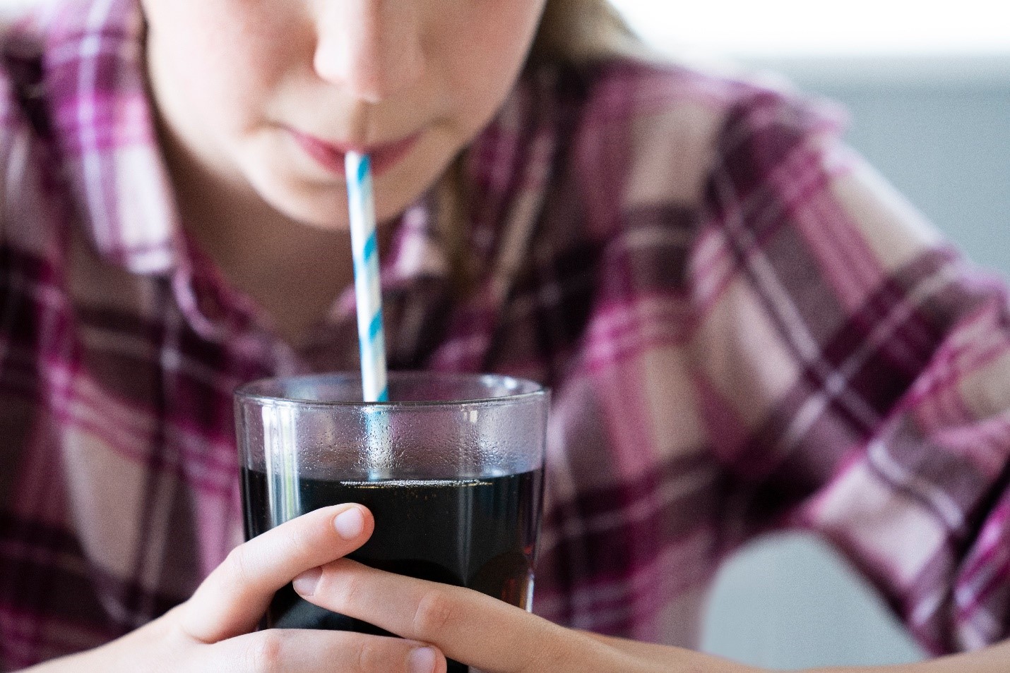 Girl drinking cola from a cup with a paper straw.