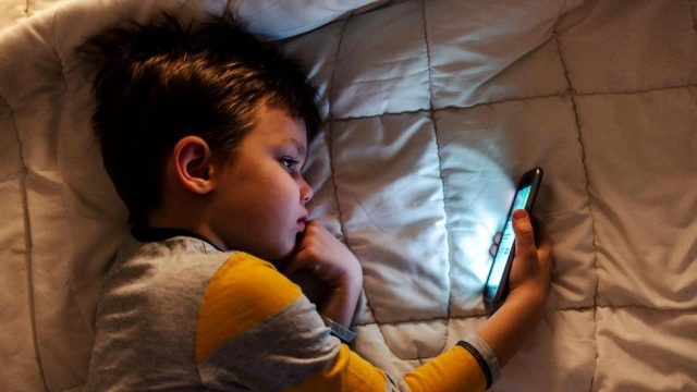 young boy looking at phone while lying in bed.