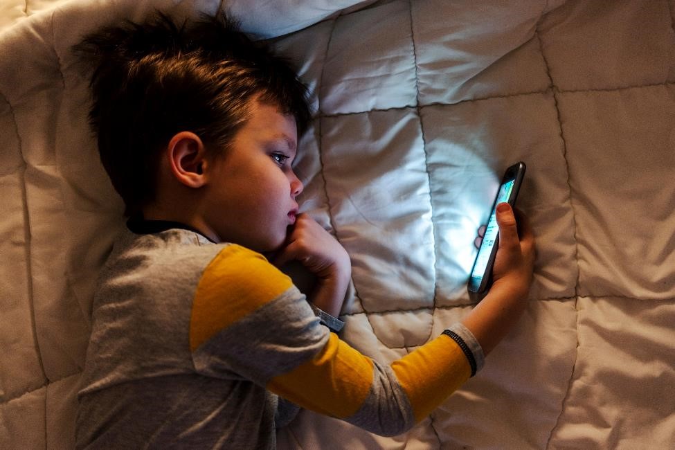 young boy looking at phone while lying in bed.