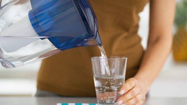 Woman pouring water into a glass from a water filter pitcher
